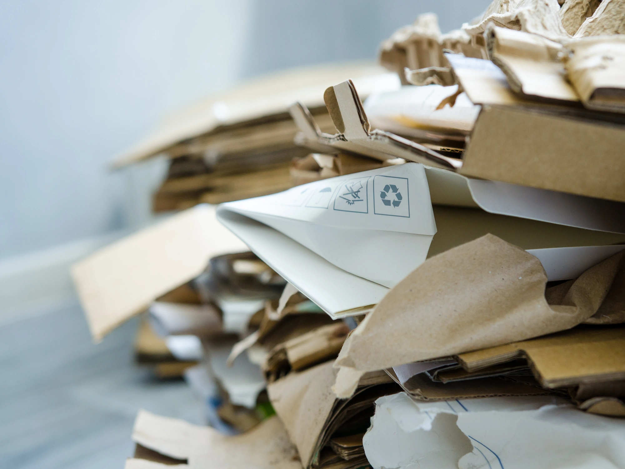 Brown mixed pile of paper with focus on recycling sign on white paper packaging.