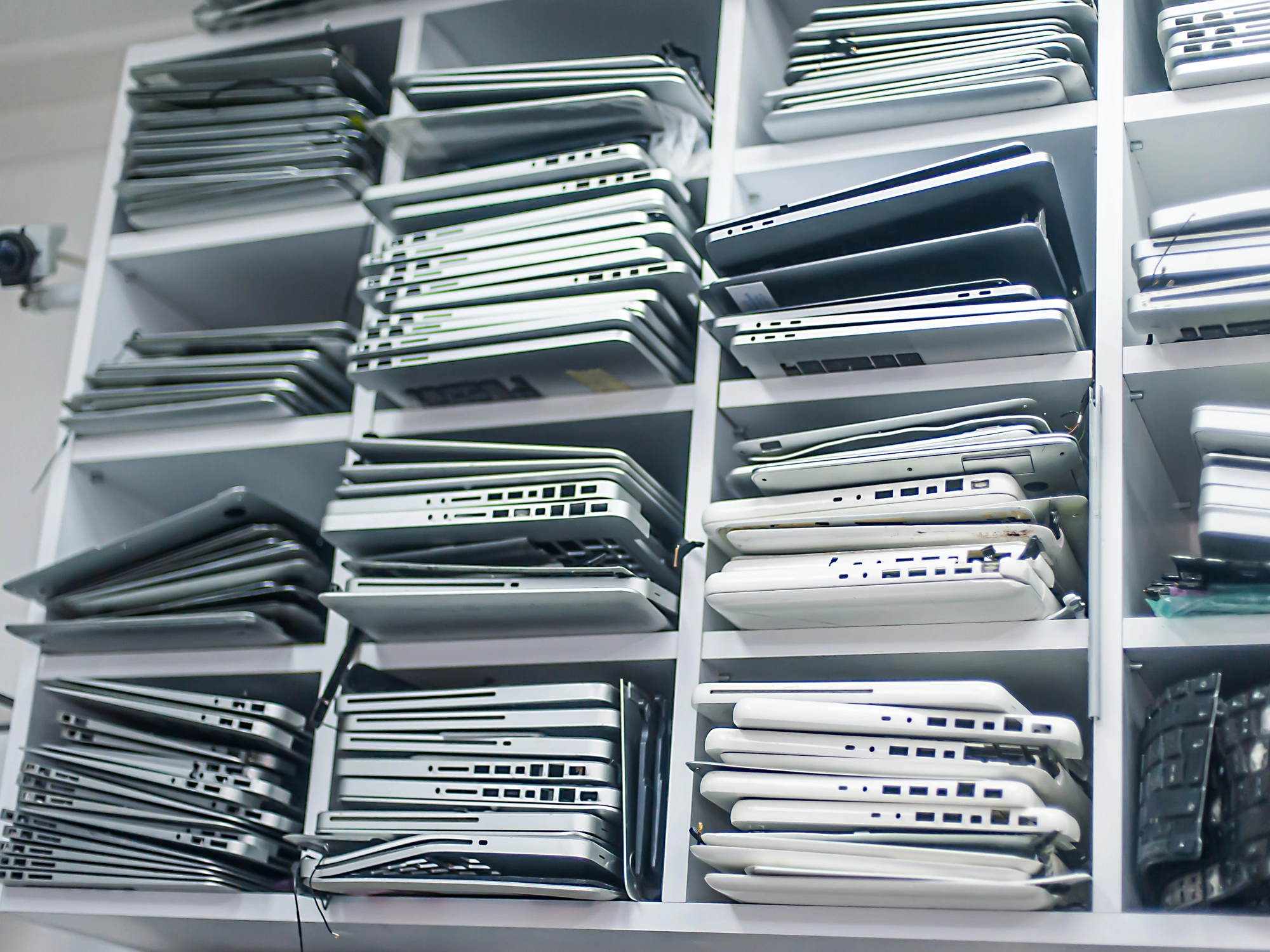 Old laptops stacked in shelving unit.