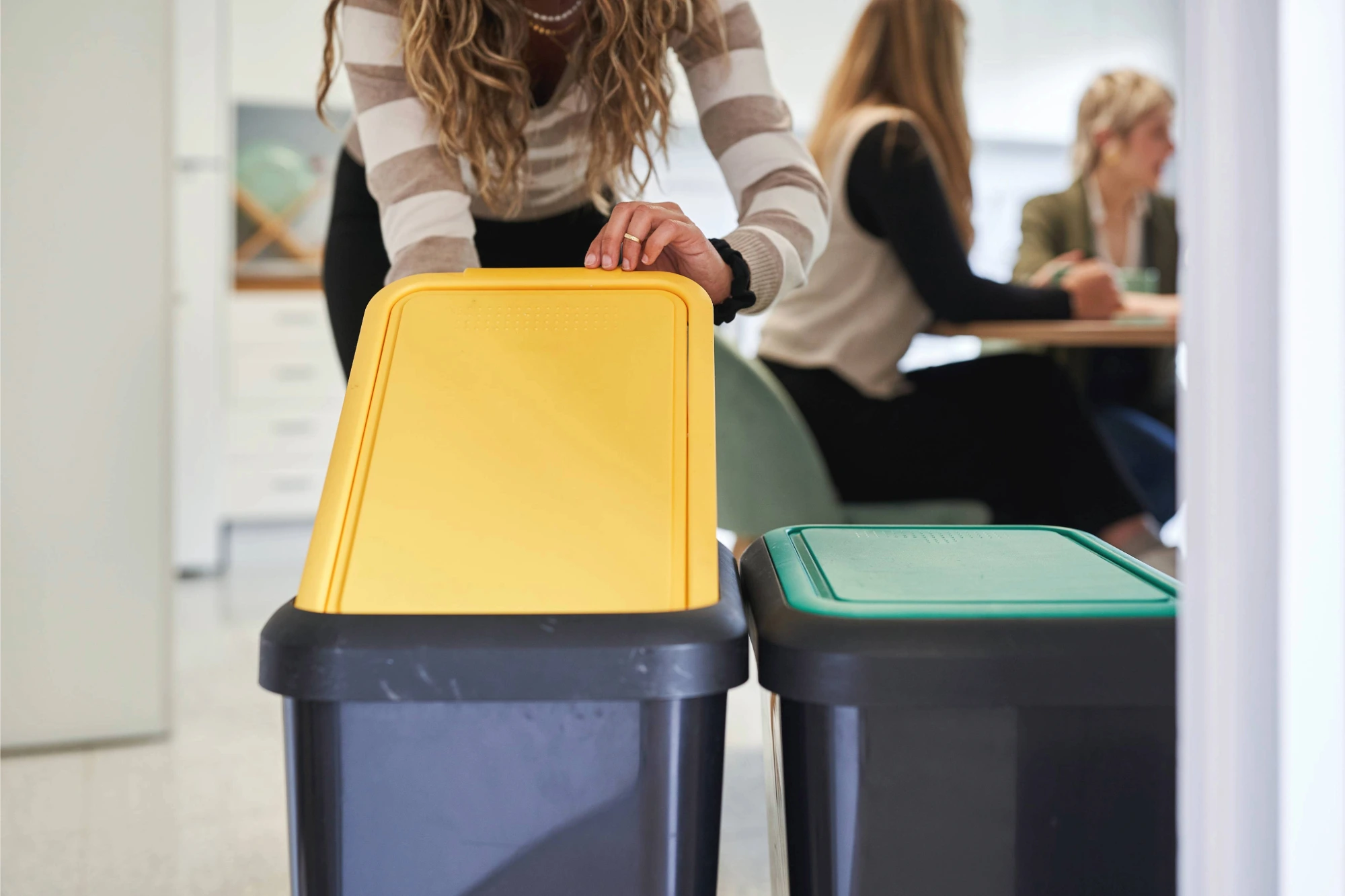 Person placing an item into a yellow-lidded recycling bin.