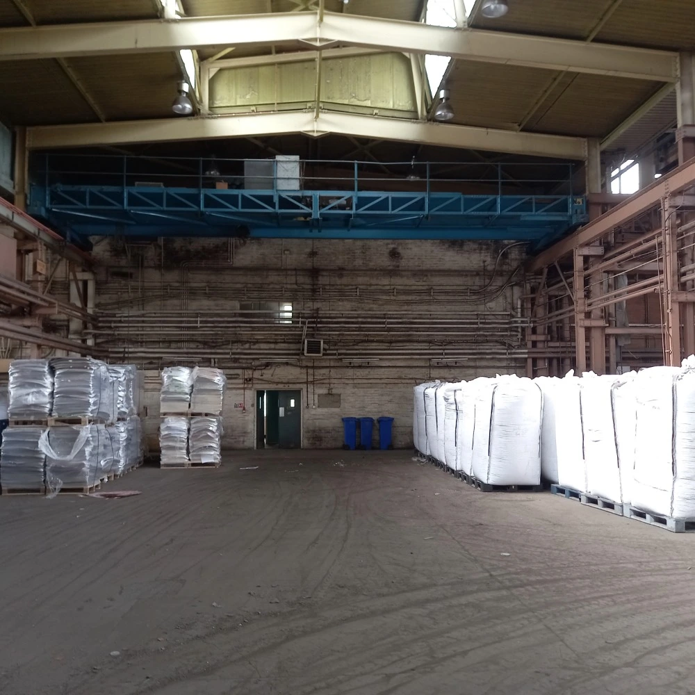 Interior of Riverdale Recycling’s warehouse showing large white bulk bags and stacked plastic-wrapped pallets stored on a dusty concrete floor.