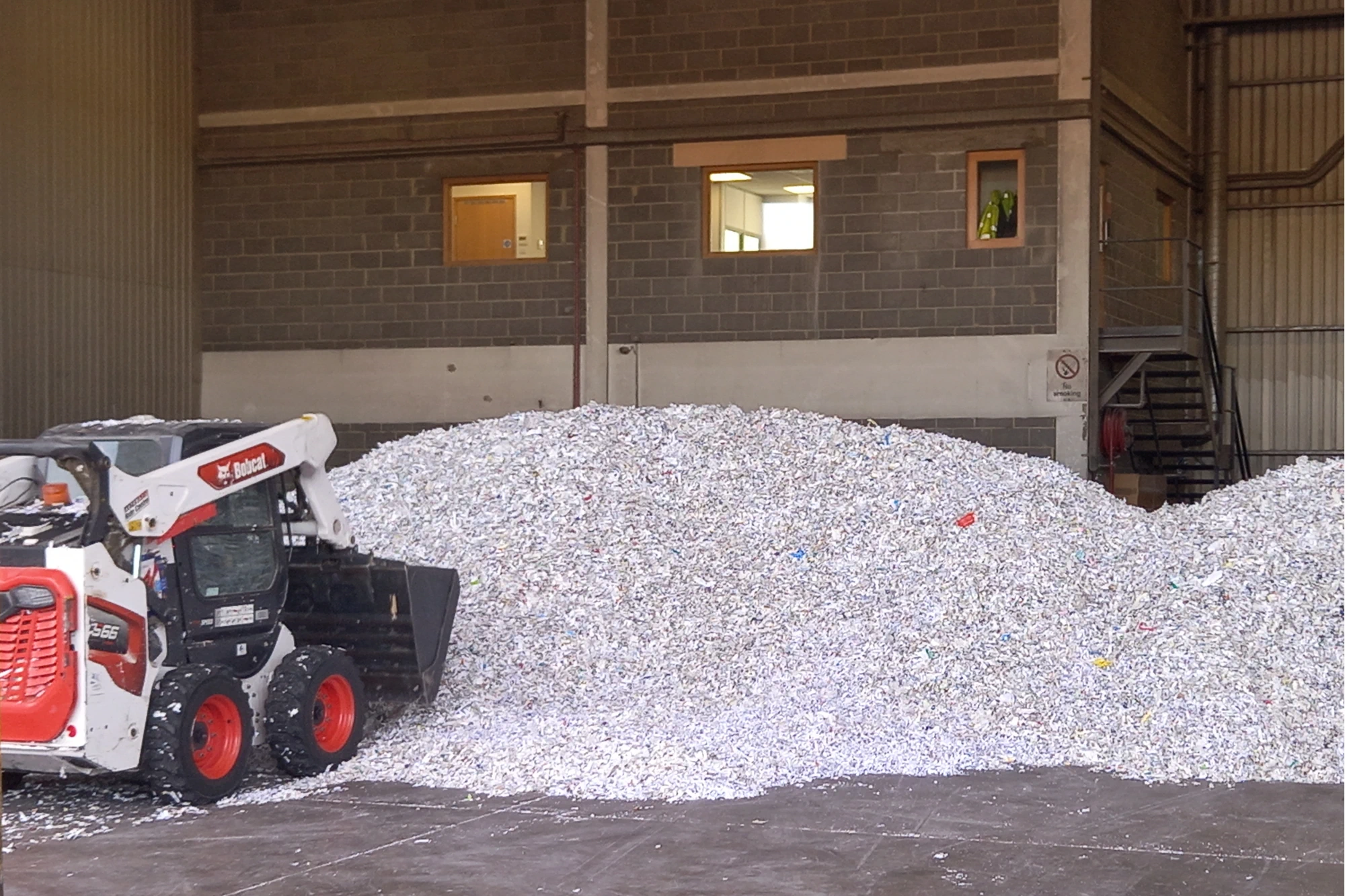 A loader next to a huge mountain of freshly shredded confidential paper inside a warehouse.