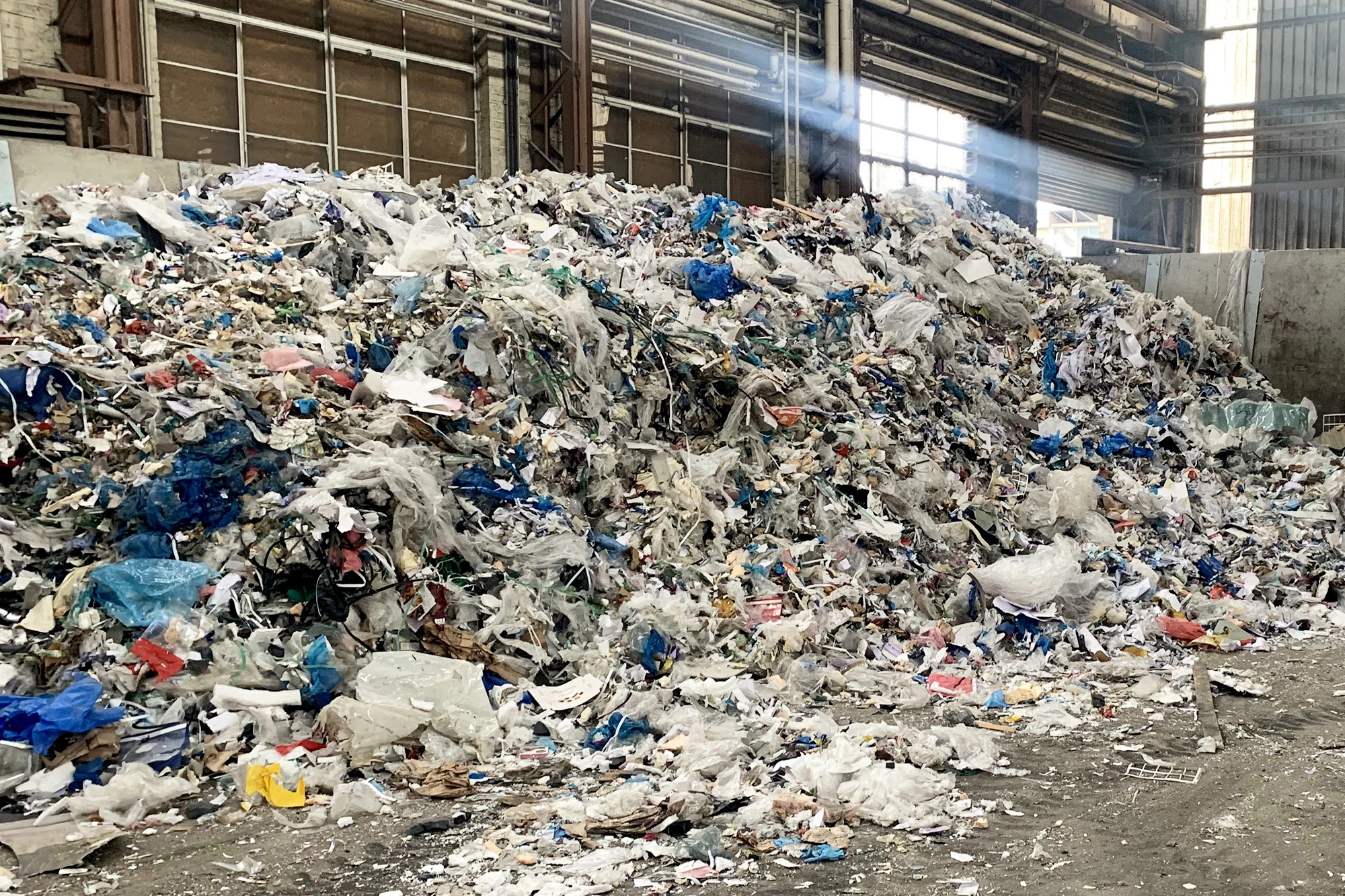 A large pile of plastic waste stacked in a warehouse setting, showcasing the storage of recyclable materials.