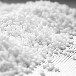 A large pile of small, white plastic resin pellets on a textured surface.