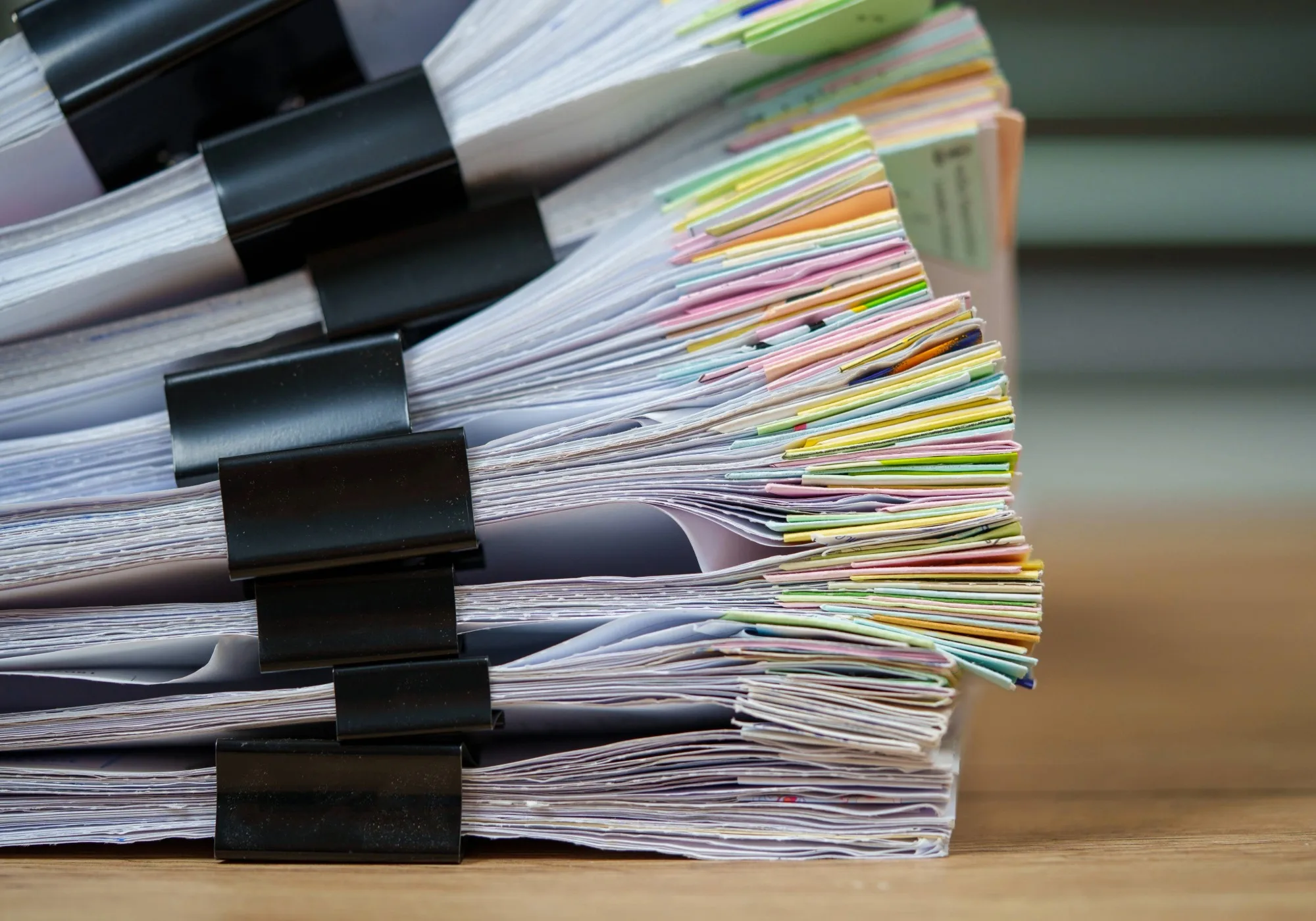 A tall stack of notes bound with metal clips on a wooden desk.