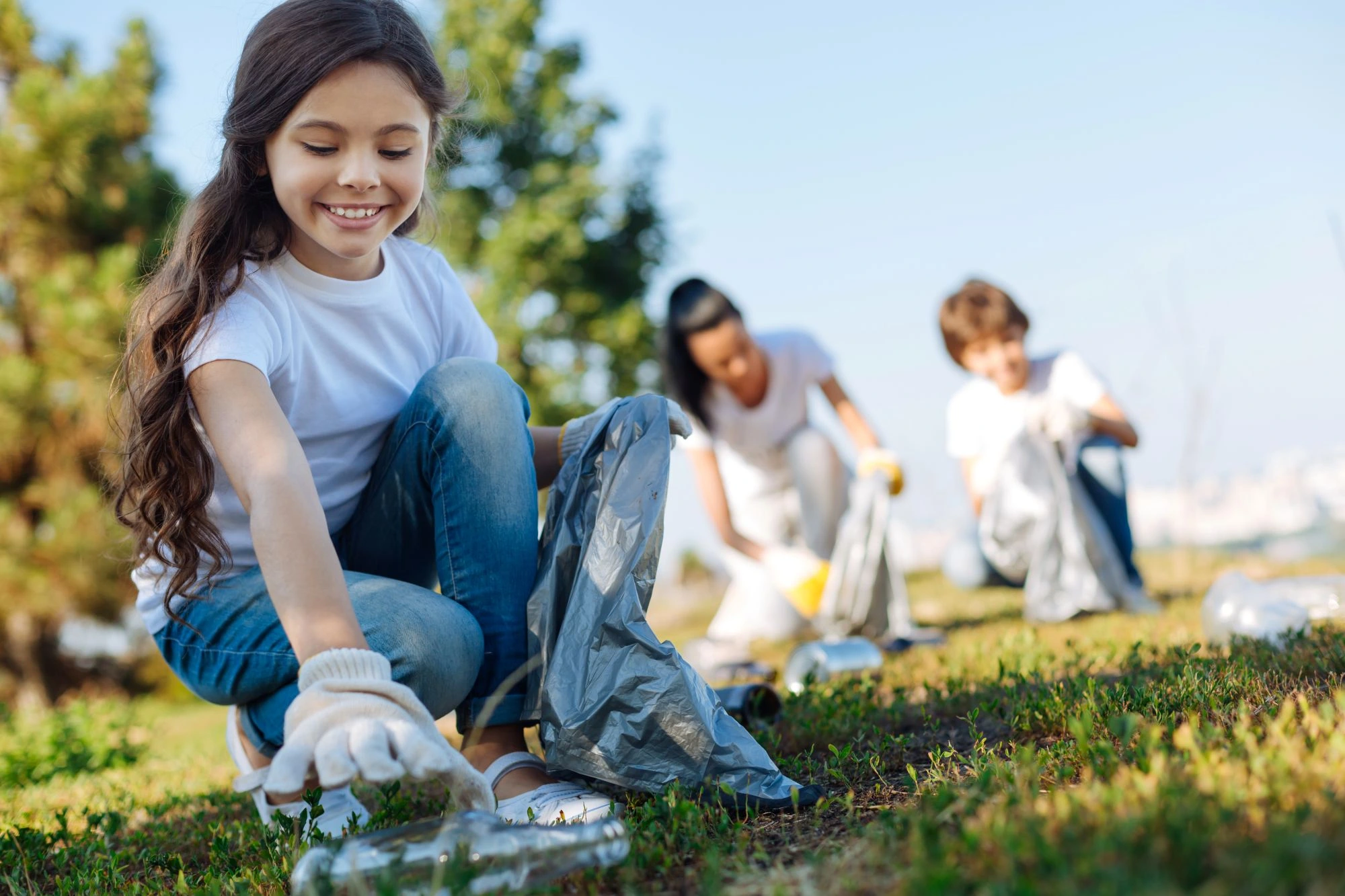 Three school students picking up litter in a local park.
