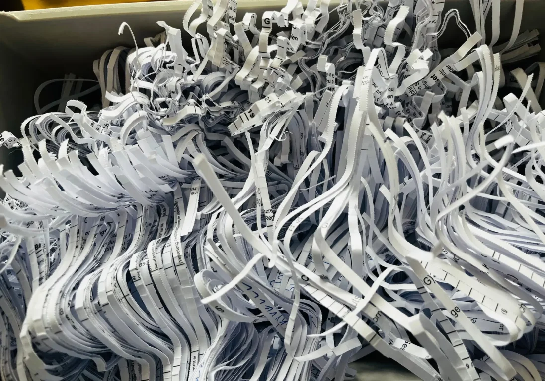 A bin filled with a tangled, chaotic pile of thin, white shredded paper strips containing fragments of black text.