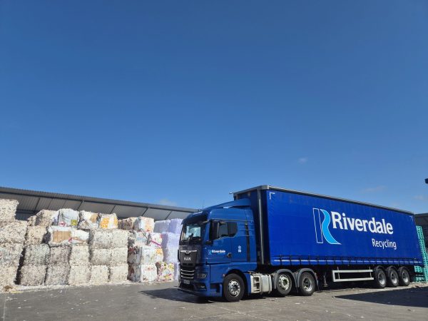 Riverdale Recycling articulated lorry parked beside large bales of recycled paper and cardboard at the company's waste recycling facility.